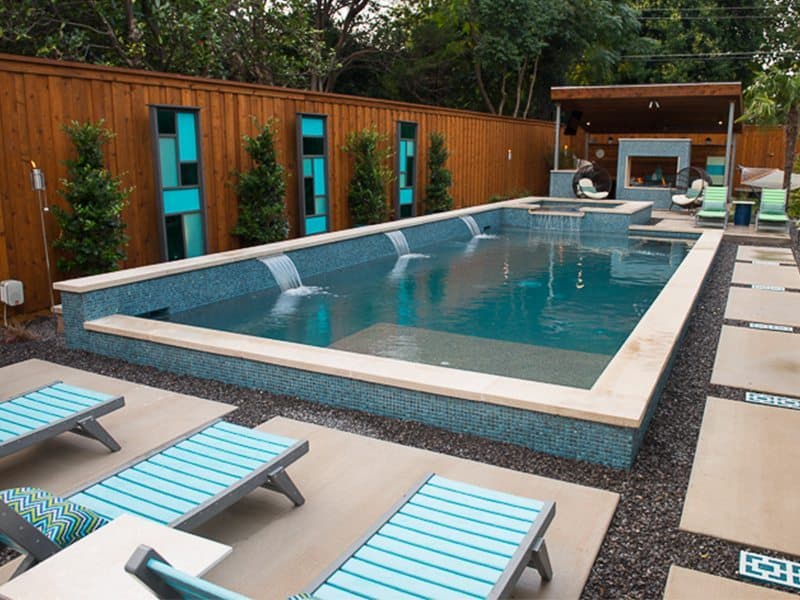 Backyard rectangle pool with water fountain feature and lounge chairs