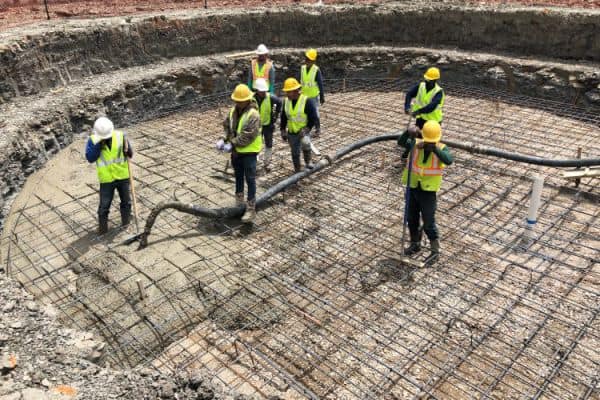 8 workers are shown pouring the concrete base of a pool under the steel rebar