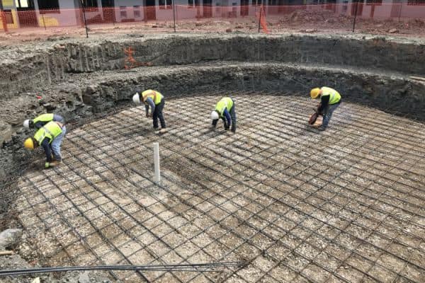 Four construction workers stand in a pool that's being built, tying the rebar