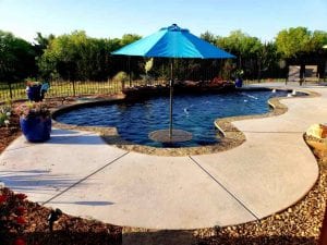 A freeform pool with an umbrella table and a custom pool deck