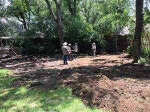 Four men stand on a dirt patch discussing a pool build