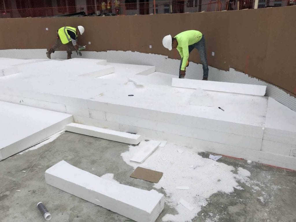 Two construction workers lay geofoam at the base of a pool