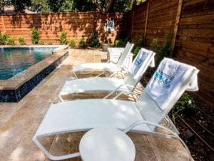 A pool deck with three poolside chairs and a small table