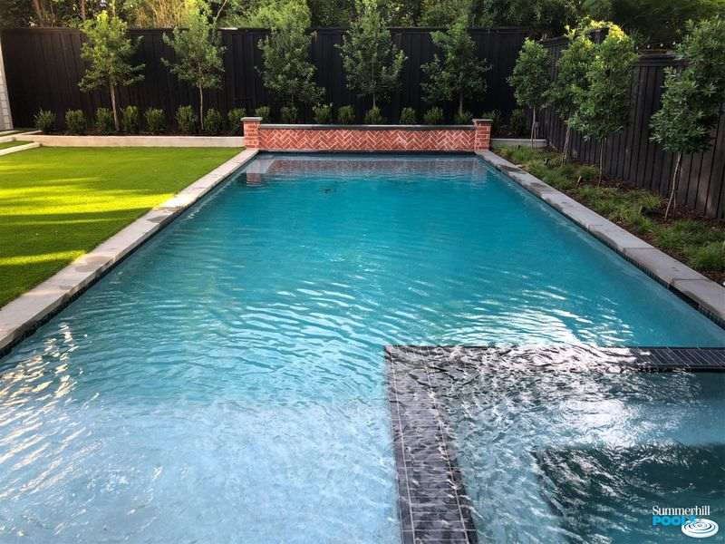 Modern pool with red brick wall.